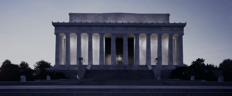 The Lincoln Memorial at dusk, floodlit between its columns, seen straight on from the steps below.