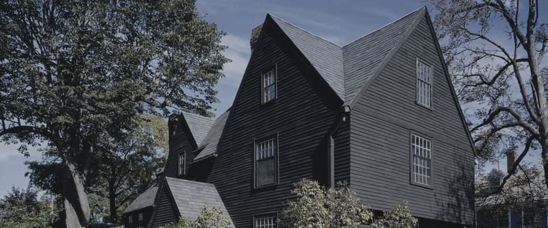 The House of the Seven Gables in Salem, its dark clapboard gables and steep roofline against a blue sky.